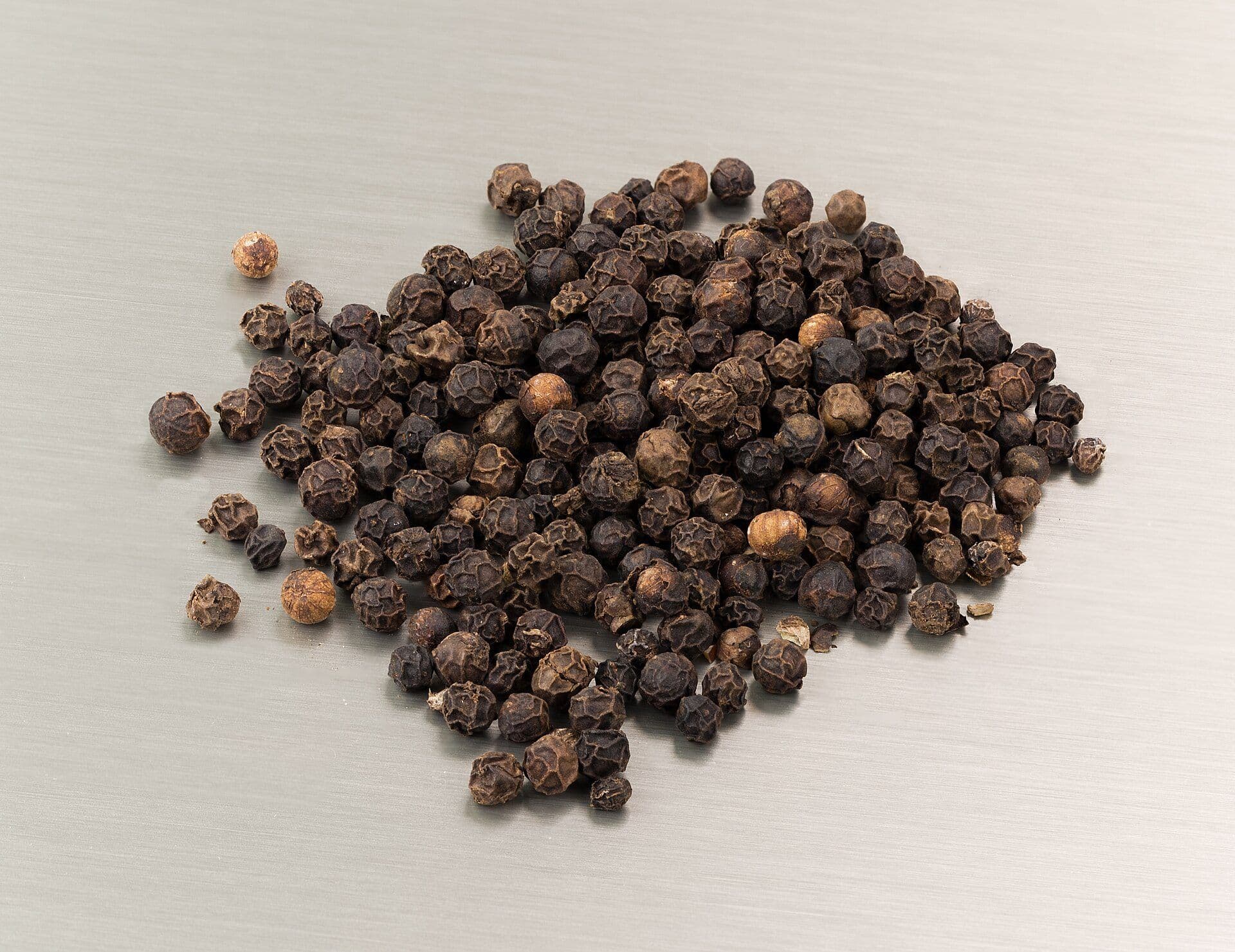 A heap of whole dried black pepper berries on a light background
