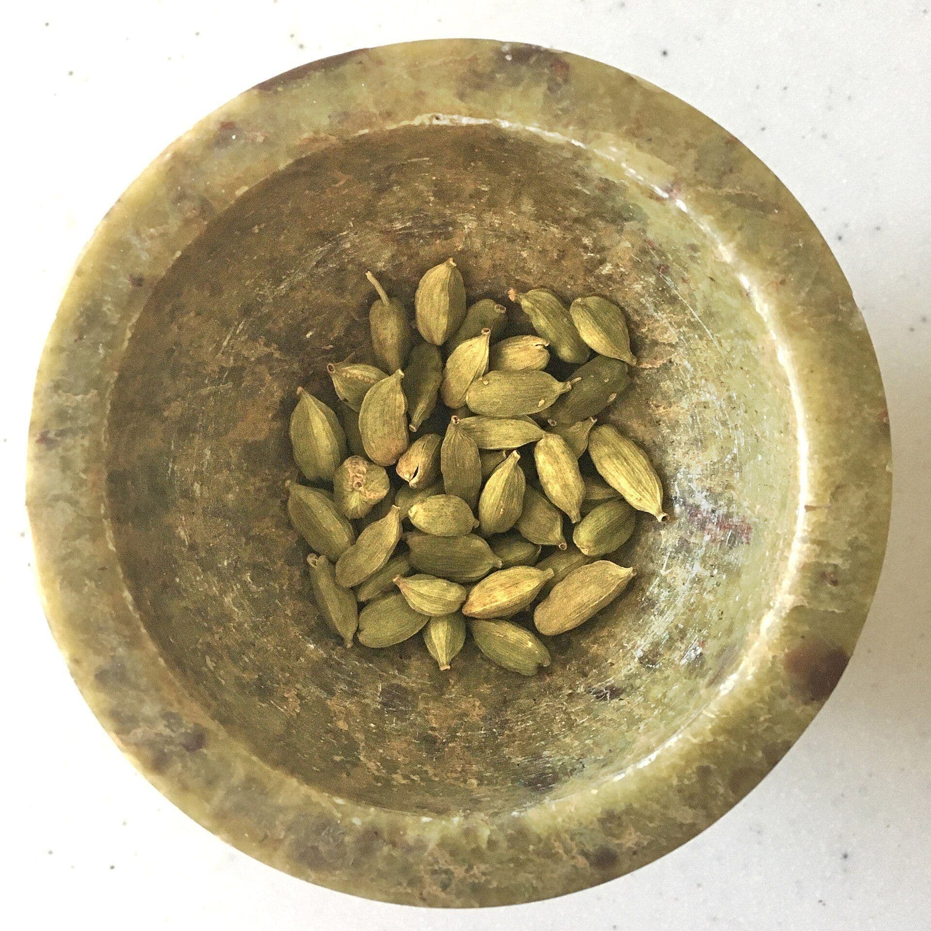 Green cardamom pods in a traditional brass bowl