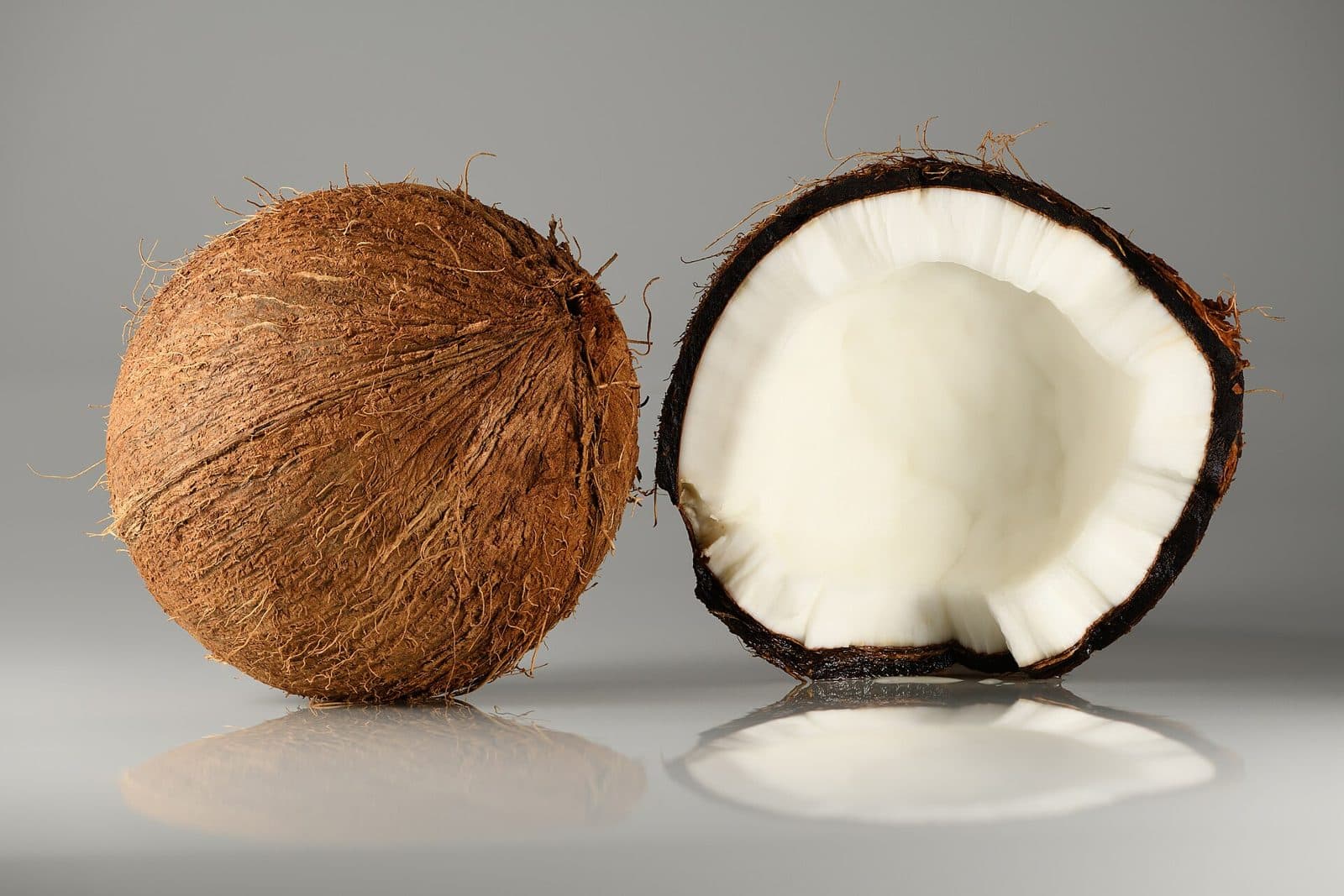 A whole brown coconut beside a coconut cracked open to show the white kernel